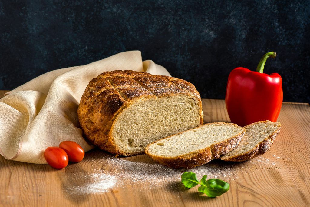 Delicious freshly baked sourdough bread with tomatoes and pepper on a rustic wooden table.